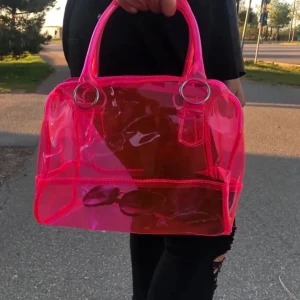 rosa genomskinlig hand väska  - Jag köpte denna i vintras och har använt den lite men nu känner jag att den inte helt passar min stil så därför säljer jag den! Det är inte mina bilder så jag kan skicka bilder ifall  någon vill! Den är i jättebra form och skit snygg! Skicka bara till mig ifall ni har några frågor!💞🥰