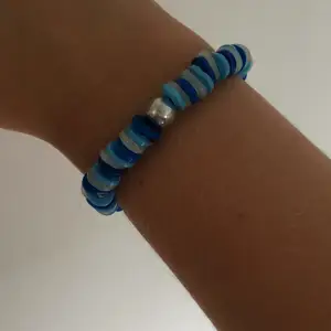 Jag säljer ett handgjort armband i färgerna mörkblå, ljusblå och vit med en rund vi pärla i mitten. 