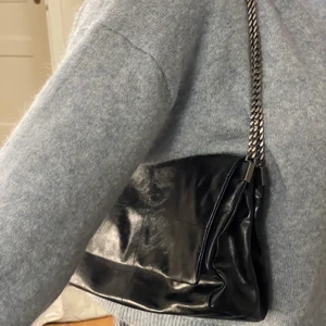 Axelväska med lock rock ZARA - Säljer denna sparsamt använda axelväska ifrån ZARA. Den är i skinnimitation och dubbla kjedjor av metalliskt slag. Väskan har ett magnetlås och tre fack på insidan där det mittersta facket har dragkjedja. Nypris 399