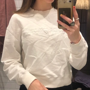 Vit sweatshirt tröja st xs - Detta är en vit sweatshirt med en vit sydd text på bröstet. Tröjan är från märket Carin Wester 