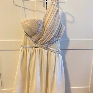 Champagne klänning - Champagnefärgad klänning med ett axelband, paljettdetaljer & tyll. Oanvänd. Storlek M. en står jag för🌸