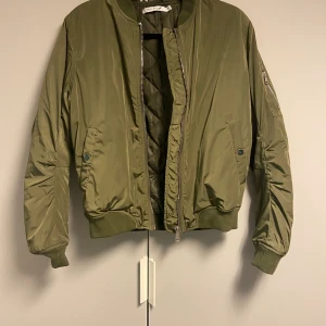 Bomberjacka - En grön bomberjacka med snygga silvriga detaljer, använd 1-2 gånger.