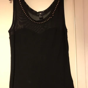 Svart fest blus - Helt oanvänd blus i ribbat material med en genomskinlig urringning i svart nät och en kant av guld pärlor