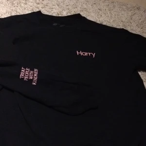 Harry Styles sweather  - Svart Harry Styles sweather med rosa broderad text på bröstet ”Harry” och ”TREAT PEOPLE WITH KINDNESS” på ena ärmen! Fint skick, köpt på Harry Styles officiella hemsida 2017. 🥰💕 Flera som är intresserade så ni får buda! budgivningen slutar idag (Fredag)  kl. 18🥰 HÖGSTA BUD: 430kr