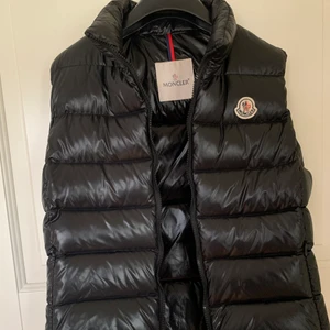 Moncler väst, svart glansig - Använd fåtal gånger och i väldigt bra skick. Storlek s/m. Säljs pga att den är för liten för mig. Köpt på nk och går att bevisa att den är äkta genom att skanna Qr-koden. Ny pris ligger på 5000kr