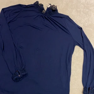 Blå tröja med lite detaljer - En mörk blå tröja med detaljer vid slutet av armen och vid kragen. Går att knäppa där bak. Lappen står fortfarande på!!