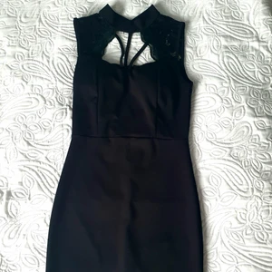 Svart festklänning  - Knappt använd, tight, svart festklänning. Spetsdetaljer upptill och halv turtleneck. Knapp baktill i nacken och näst intill osynlig dragkedja längs med ryggen. Består till 95% av polyester, dvs strechigt material. 