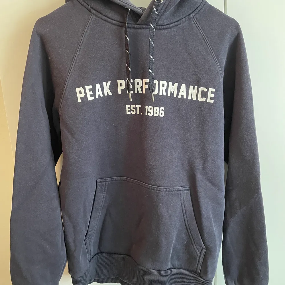 Mörkblå Peak performance hoodie i bra skick förutom att trycket börjar släppa lite därav priset. Storlek S. Vid köp av fler plagg fixar vi ett schysst paketpris!😊. Hoodies.