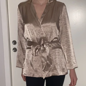 Kavaj i skimrande rosé - Kavaj med skärp i skimrande rosé. Saknar en knapp framtill, i övrigt mycket bra skick