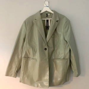 PU-läder / Vegansk fakeläder KAVAJ - LARGE - Mintgrön - H&M - STORLEK LARGE - KAVAJ  Oanvänd med prislapp kvar.  Originalpris: 499:-  Enkelknäppning, två knappar, lite oversized.