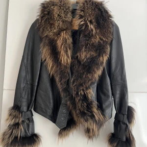 Läderjacka med päls - Läderjacka i päls. Unik då detta är den enda som finns. Den köptes på en modevisning för några år sen & har endast använts ett par gånger sen dess. I fint skick, saknas en liten metallring runt ett av hålen i bältet (syns knappt). Äkta läder & päls