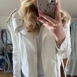 Vit skinnjacka  - Vit skinnjacka ifrån prittylittlething. Inte min still längre därför säljs den. Inga defekter. Har även ett bälte i midjan 