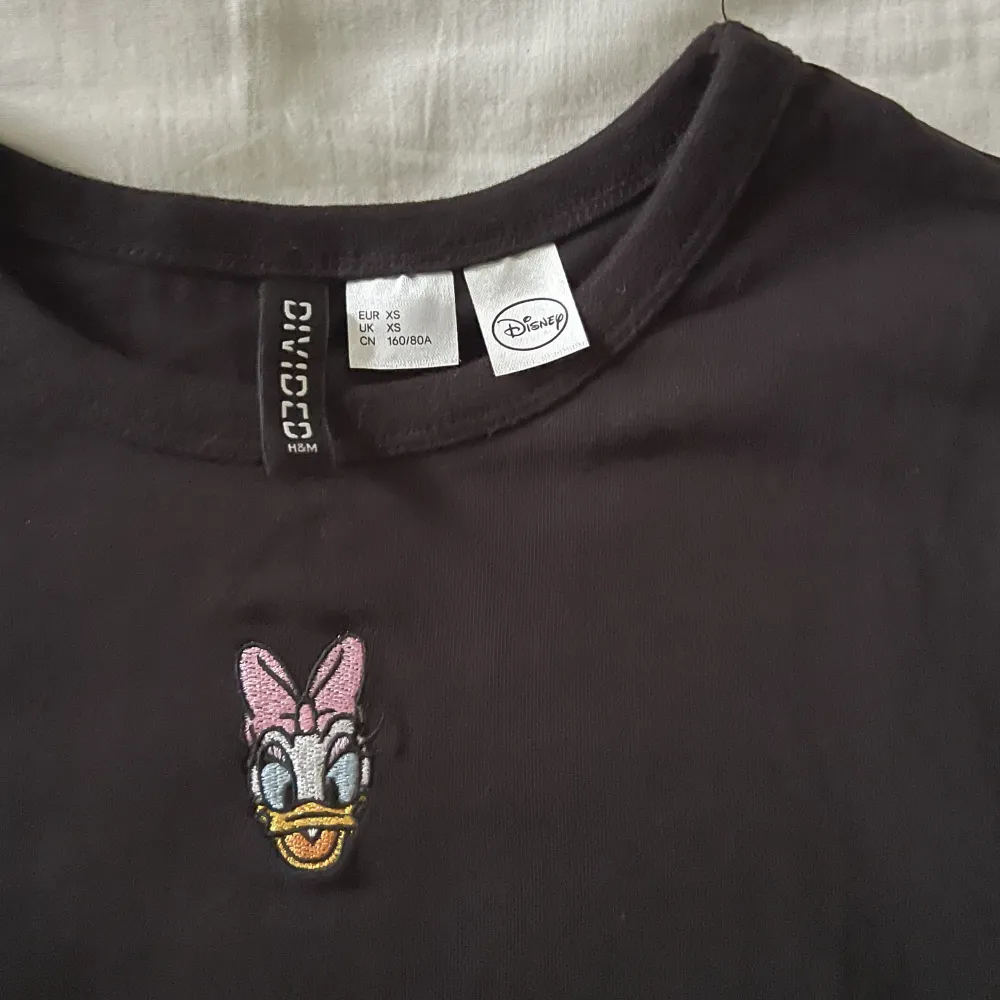 Supersöt svart T-shirt med Daisy duck broderat på framsidan. Aldrig använd, så nyskick! Storlek XS men stretchigt material så passar även S🫶💕. T-shirts.