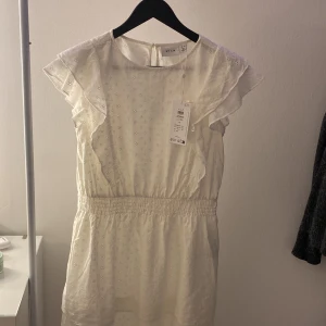 Vit volang klänning  - Säljer denna helt oanvända klänningen från vila. Prislapp finns kvar💗  Perfekt att ha till skolavslutningen💕