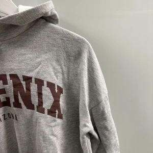 Luvtröja - Grå tröja med luva, med snörning i midjan. Strl s.