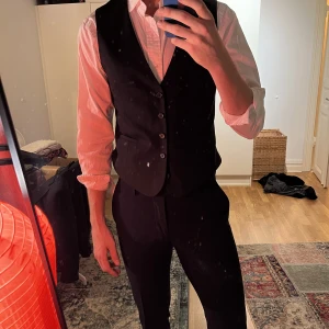 Kostymväst svart J.Lindberg - Säljer denna eleganta svarta kostymväst från J.Lindberg. Med sin slim fit passform ger den en modern och stilren silhuett, perfekt för formella tillfällen eller när du bara vill lyfta din outfit till nästa nivå.