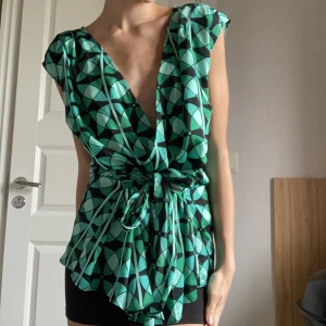 Blus -  Super snygg v-ringad grön blus med olika nyanser av grön, blå och svart. Man kan själv välja att knyta snören till en rosett längst fram eller bak. Köpt från märket Anntaylor. Nyttskick!💚
