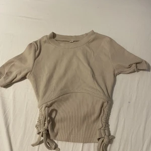 Beige T-shirt  - Beige t-shirt med knyten på sidan som går att schystera längden stl:S