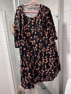 Marimekko bomulklänning 3XL - Marimekko bomulklänning 3XL  Olivia Lemmings  Orange blommor i svarta bas  Bomull, lite elastisk   Anvant bara ett par gånger, så jättefint skick   Storlek 3XL (passar kanske bäst runt storlek 48-50)