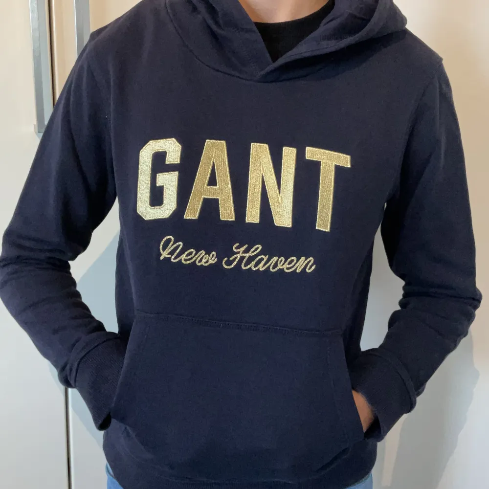 Mörkblå luvtröja med guldbrodyr från Gant sparsamt använd i gott skick. 146-152 /11-12 år.. Hoodies.