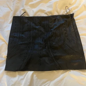 Svart skinnkjol  - Svart skinnkjol med flätade detaljer fram. Passar M! 