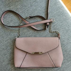 Gammelrosa handväska/axelremsväska  - Fin väska i gammelrosa. Märke Anna Field. Inköpt på Zalando. Aldrig använd.  Ett större fack, ett mindre utan dragkedja samt ett litet fack med dragkedja. Stora facket kan stängas med dragkedja, väskan knäpps sedan med magnetlås