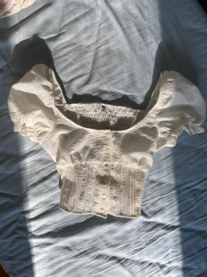 söt topp - Croppad vit/crémefärgad kortärmad topp/blus som man knäpper fram, tight i midjan och lite pösig i byst och ärmar. Jättefin urringning🐚