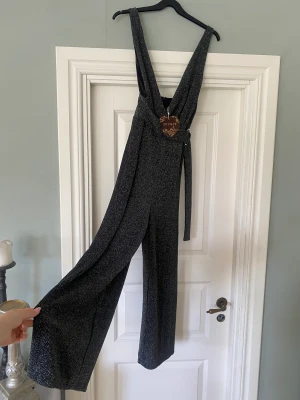 Oanvänd glittrig byxdress - Svartglittrig oanvänd byxdress köpt från Missäy. Kort i benen samt ganska öppen framtill vid brösten. Nypris 500 kr.
