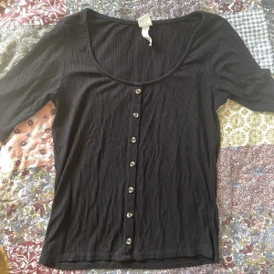 Svart t-shirt - Svart t-shirt med knappar. Ribbat tyg. 