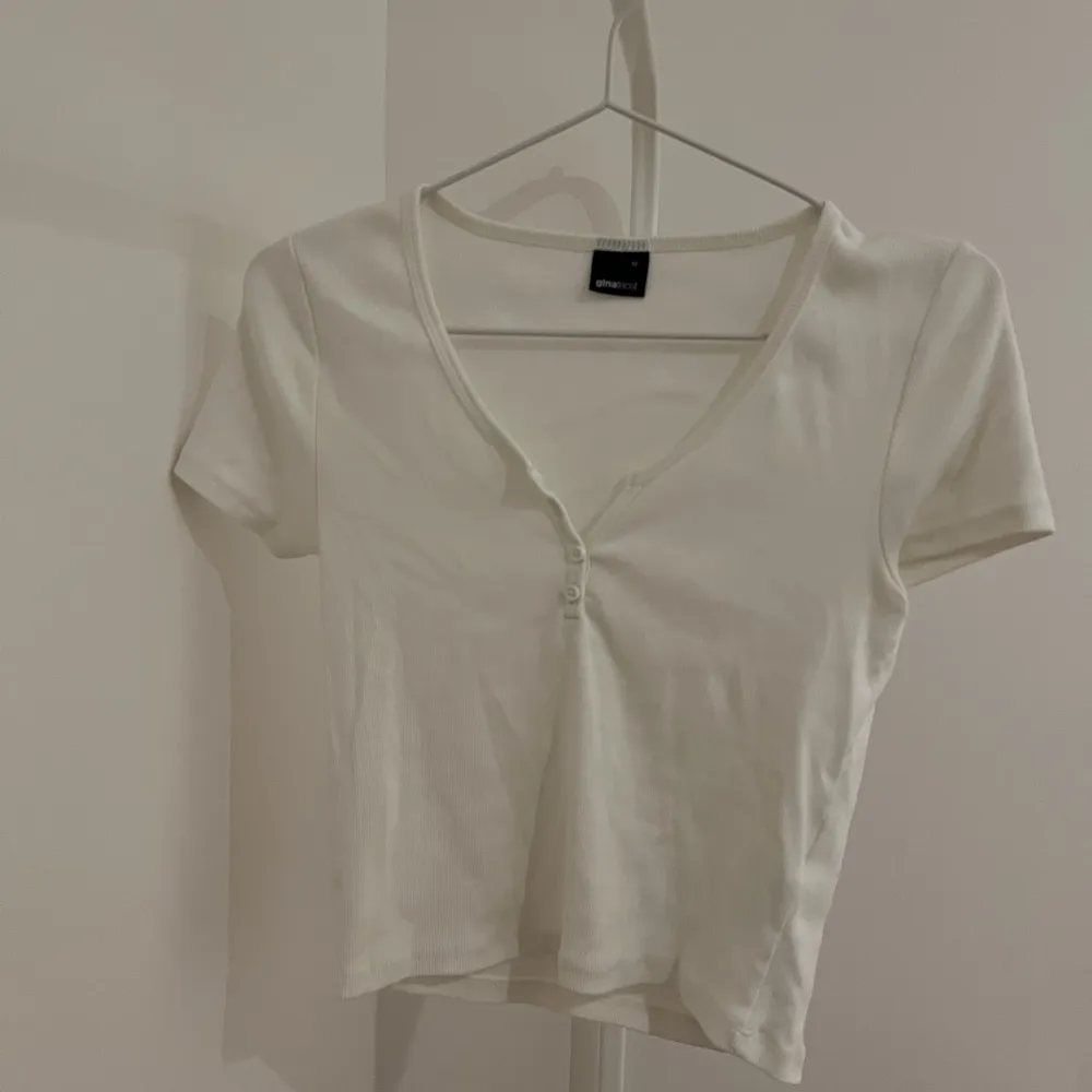 Vit croppad topp/T-shirt från Gina Tricot. Saknar översta knappen, antagligen varit så från början då jag inte ens visste att där skulle va en knapp. Knappt använd, fint skick🤍. T-shirts.