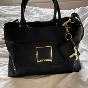 Steve Madden väska - En svart Steve Madden väska med guld detaljer, medföljer axelrem och liten plånbok. Har tre stora fack och en yttre mindre ficka