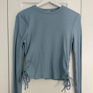 blå långärmad tröja med knytning💙 - Blå, ribbad, kortare tröja med knytning på sidan!💙 Använd 1 gång, storlek M, från NAKD, betalning sker via Swish, köparen står för frakten, står ej för påstens slarv!🤍