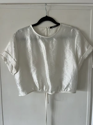 Glansig topp - En vit glansig croppad topp med snörning i storlek 36. Toppen är från Ginatricot och har använts försiktigt, fint skick. 
