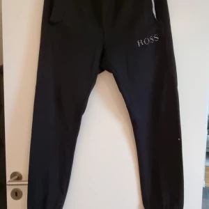 Hugo boss mjukisbyxor - Svarta mjukisbyxor, detaljer i silver/grått, reflekterande mönster på baksidan. Snöre saknas, en bakficka. Fint skick. Finns tillhörande hoodie.