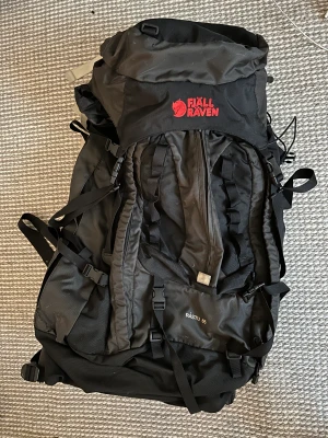 Fjällräven Råstu 65 - Litet hål på sidan, se bild. Annars kanon. Perfekt vandringsryggsäck.