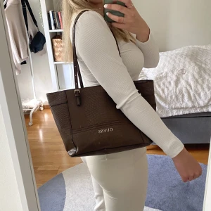 Guess handväska - Supergullig brun Guess handväska! Längd: 28 cm, bredd 14 cm, höjd 24 cm🌸 Det syns att väskan är använd, men den är fortfarande i fint skick🫶
