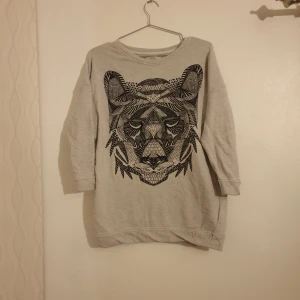 Tröja med tiger tryck och 3/4-ärmar - Ljust beige tröja med tryck. Modell med sömmar som ser lite "slitna ut".  Gott skick 