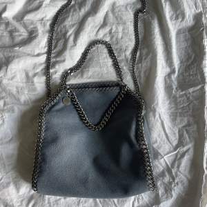 Säljer denna blå/gråa Stella McCartney Falabella väskan! 🤩Nypris idag är 10180kr. Köpt 2021 men sparsamt använd och väldigt fint skick. Kvitto medföljer! Denna färgen går inte att köpa ny längre.  Mått: 26,5 x 23,5 x 10cm