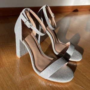 Silverglittriga klackskor  - Superfina klackar som passar till bal, fest, bröllop eller vilken tillställning som helst. Storlek 37, höjd 9,3cm. De är wide fit, från new look, asos. Helt oanvända. Säljs pga beställd i fel storlek. Köparen står för frakten. 