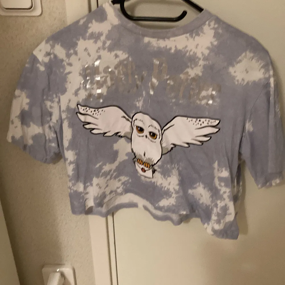 Harry Potter t-shirt från hm. Det står Harry Potter med silverfärgad och hans Uggla Hedwig på tröjan. Den säljs inte längre. Den är bred och kort och stor i storleken men ingen magtröja direkt. Den är ner till armbågarna. Den är blå och vit.. T-shirts.