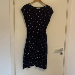 Perfekt strandklänning  - Perfekt strandklänning i mörkblått med vit palmer på. Finns möjlighet till att knyta klänningen vid midjan med ett tillhörande skärp. Klänning är gjord av bomull. 