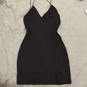 Svart klänning  - Svart tunn (men inte genomskinlig) klänning. Den har en mini slits och djup urringning. Spagettiband som korsar i ryggen. Tight/ figursydd. Den är oanvänd. 