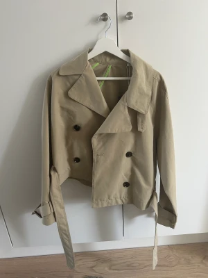Kort trenchcoat - Kort trenchcoat. Helt oanvänd, säljer för att jag köpt en liknande så den kommer ej till användning. Ordinariepris 699kr
