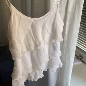 Volanglinne - Crémefärgat asymetriskt linne med volanger! Aldrig använt 