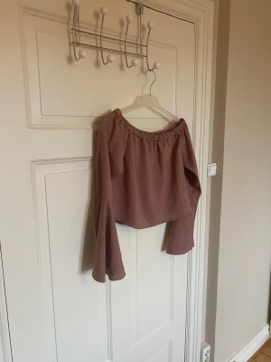 Topp från NA-KD  - Säljer denna söta toppen från NA-KD. I fint skick. Storlek S. Med trumpet-ärmar. Off-shoulder. Rostbrun.
