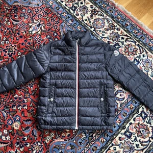Mocler barn höstjacka - En moncler jacka till barn. Använt ett fåtal gånger och säljs för att den blivit för liten. Kvitto finns samt en dustbag. (Man kan även fälla ut en luva till jackan). 