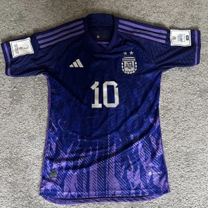 Argentina tröja VM 2022 - Argentina bortatröja från fotbolls VM i Qatar 2022 där de gick och vann. Tröjan har alla patches på tröjärmarna och Messi 10 på ryggen. Detta är även spelarverisionen som även är den dyrare men också bättre varianten. Den är oanvänd, pris kan diskuteras.
