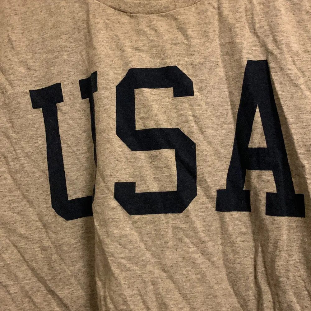 En grå t-shirt med trycket USA på. T-shirts.