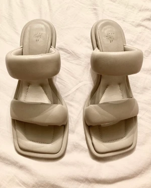 Mules, skor H&M - Mules i läderimitation. Strl 37, ljusgrå, klackhöjd 6,5 cm, mjuka vadderade remmar. Helt oanvända! Köparen betalar frakt.
