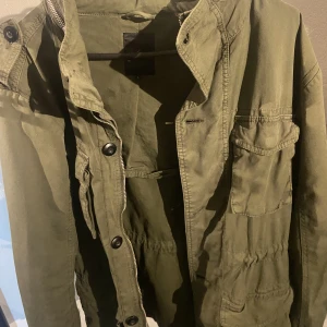 NEW look M65 jacka - NEW look vintage M65 jacka en praktisk jacka med inbyggd luva och 4 fickor. Dragsnodar i midjan för justering och dragkedja och knappar. Jackan är använd sparsamt och inga tecken på skador 